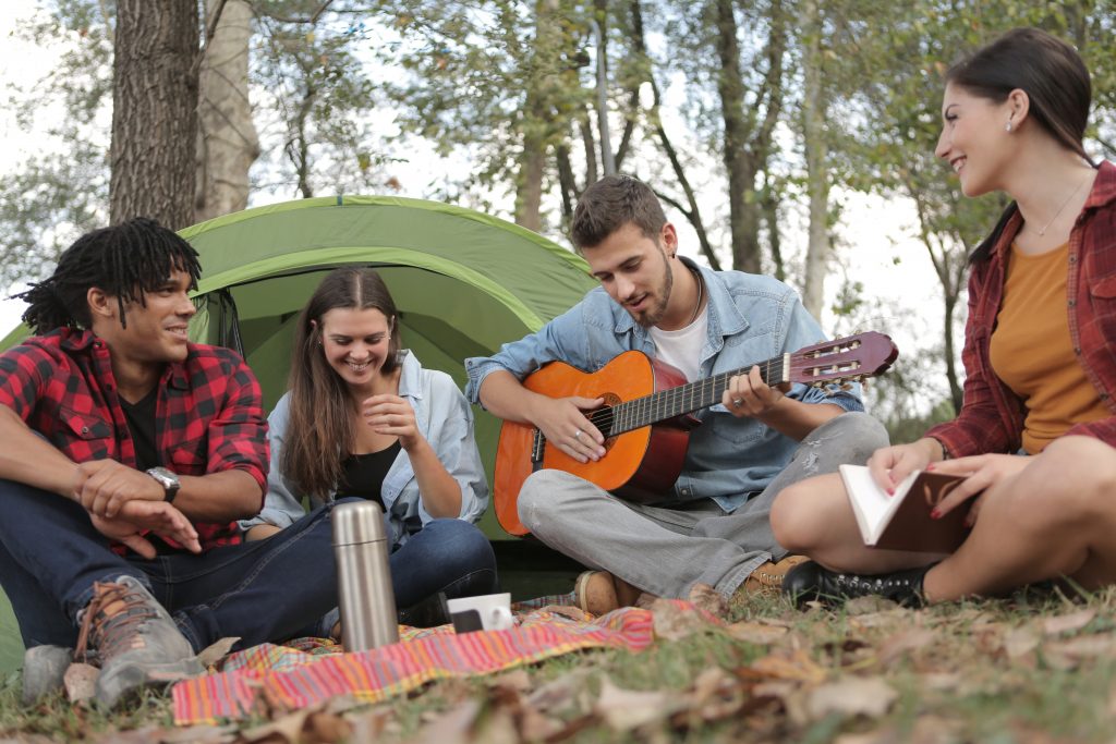 Four young adults playing guitar at over nighttcampsite